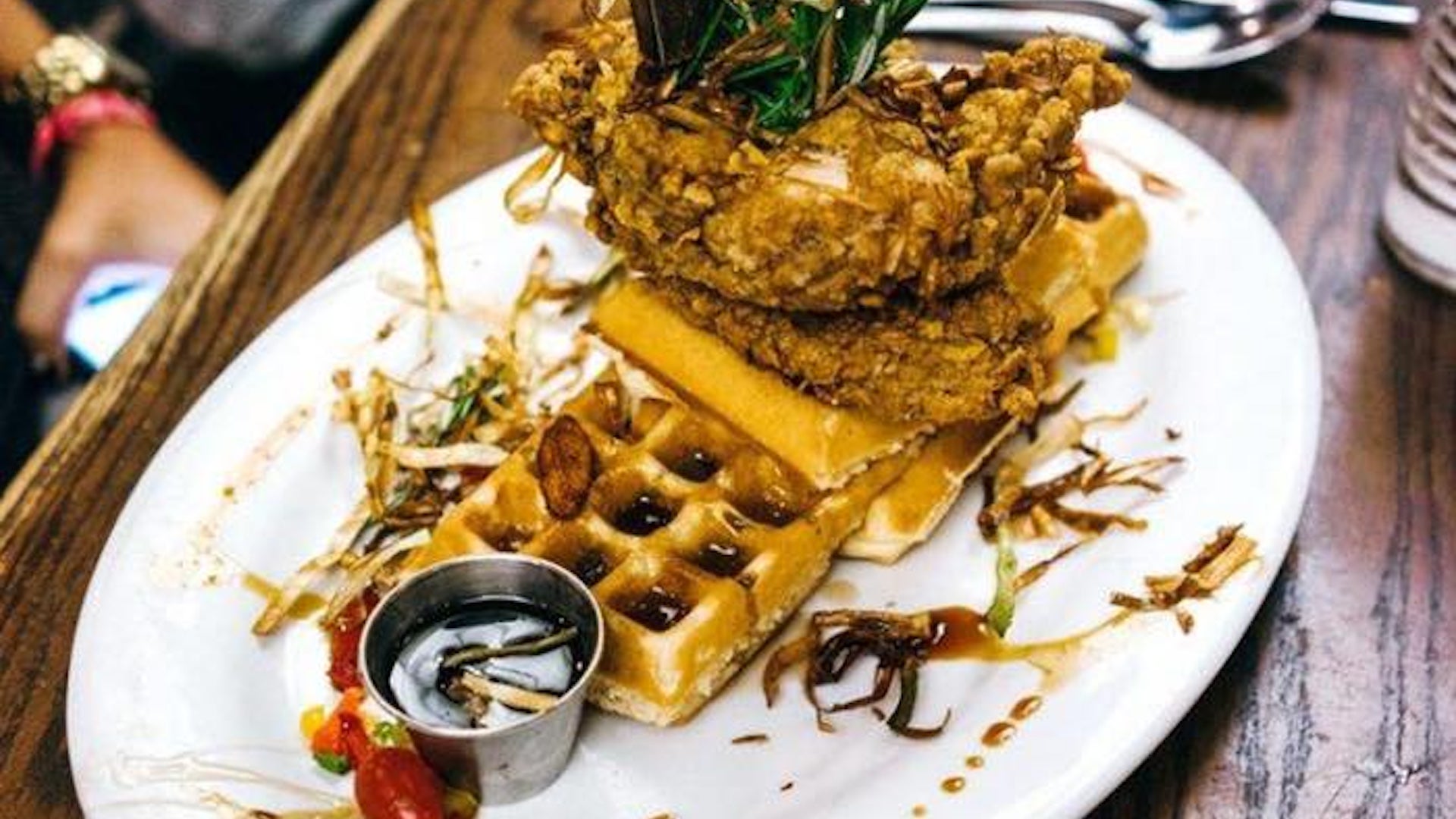 Chicken and waffles on a white plate with a side of syrup