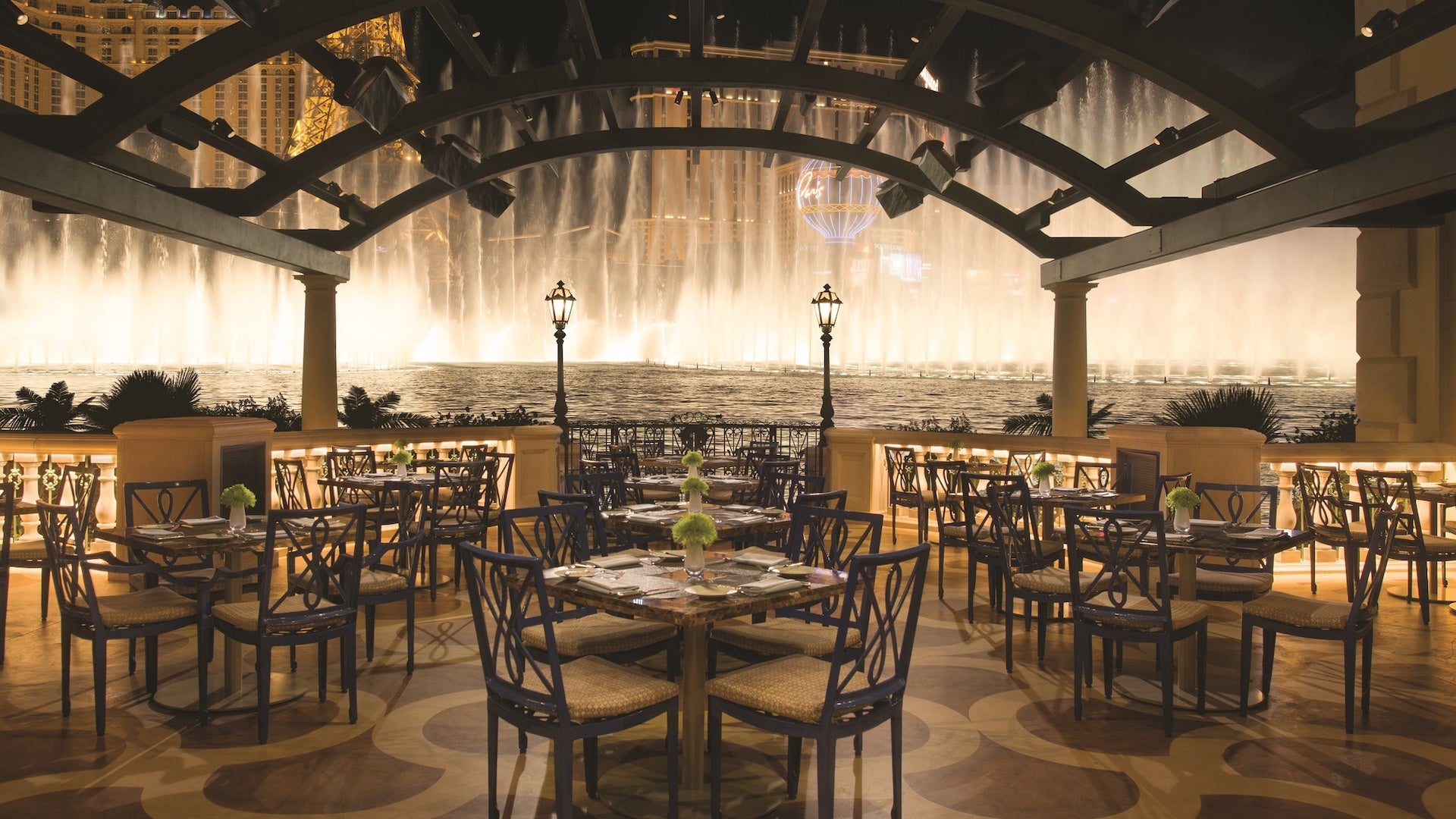 Wide shot of a dining area under an awning with the Bellagio fountains in the background