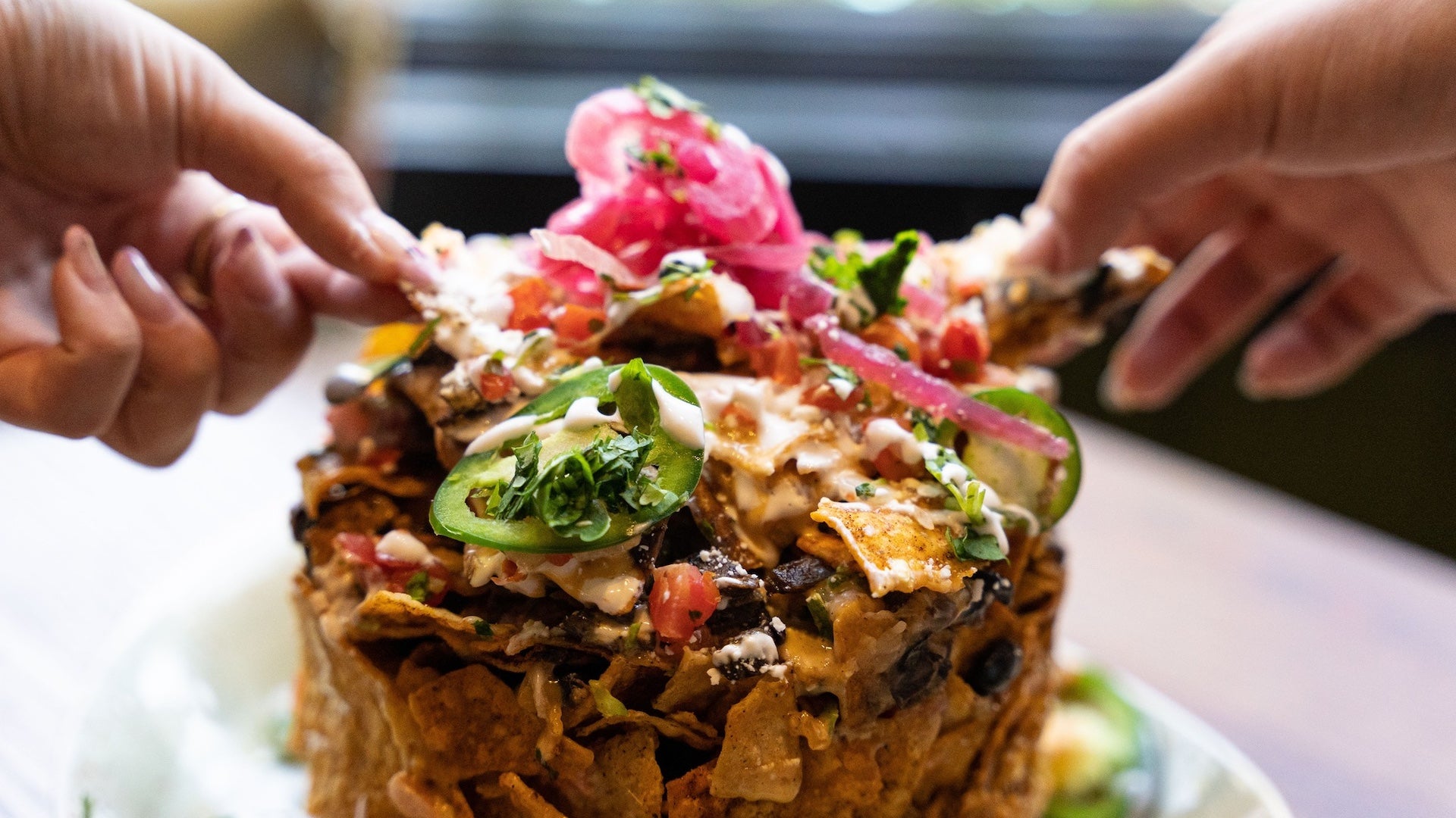 Two hands pulling apart a nacho stack