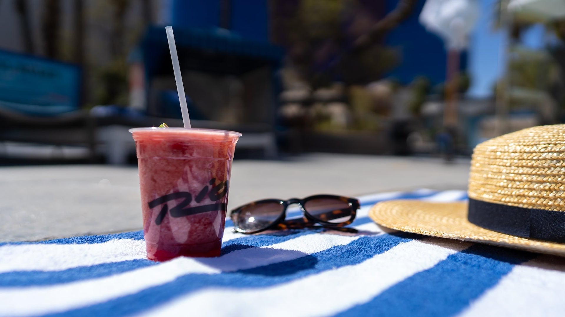 Frozen drink on a blue and white striped towel with a pair of sunglasses and a hat sitting next to it