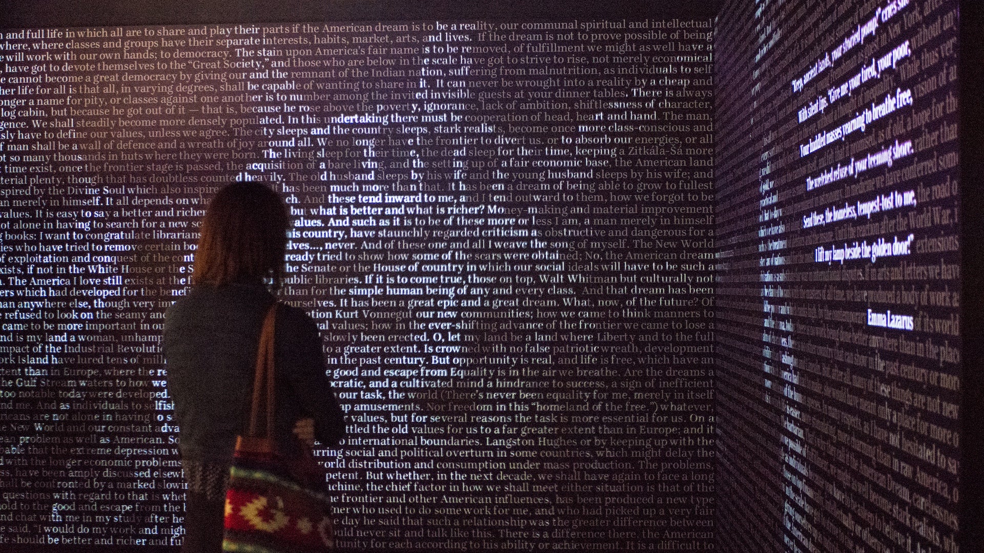 A person standing near a wall filled with words to create a picture of the Statue of Liberty