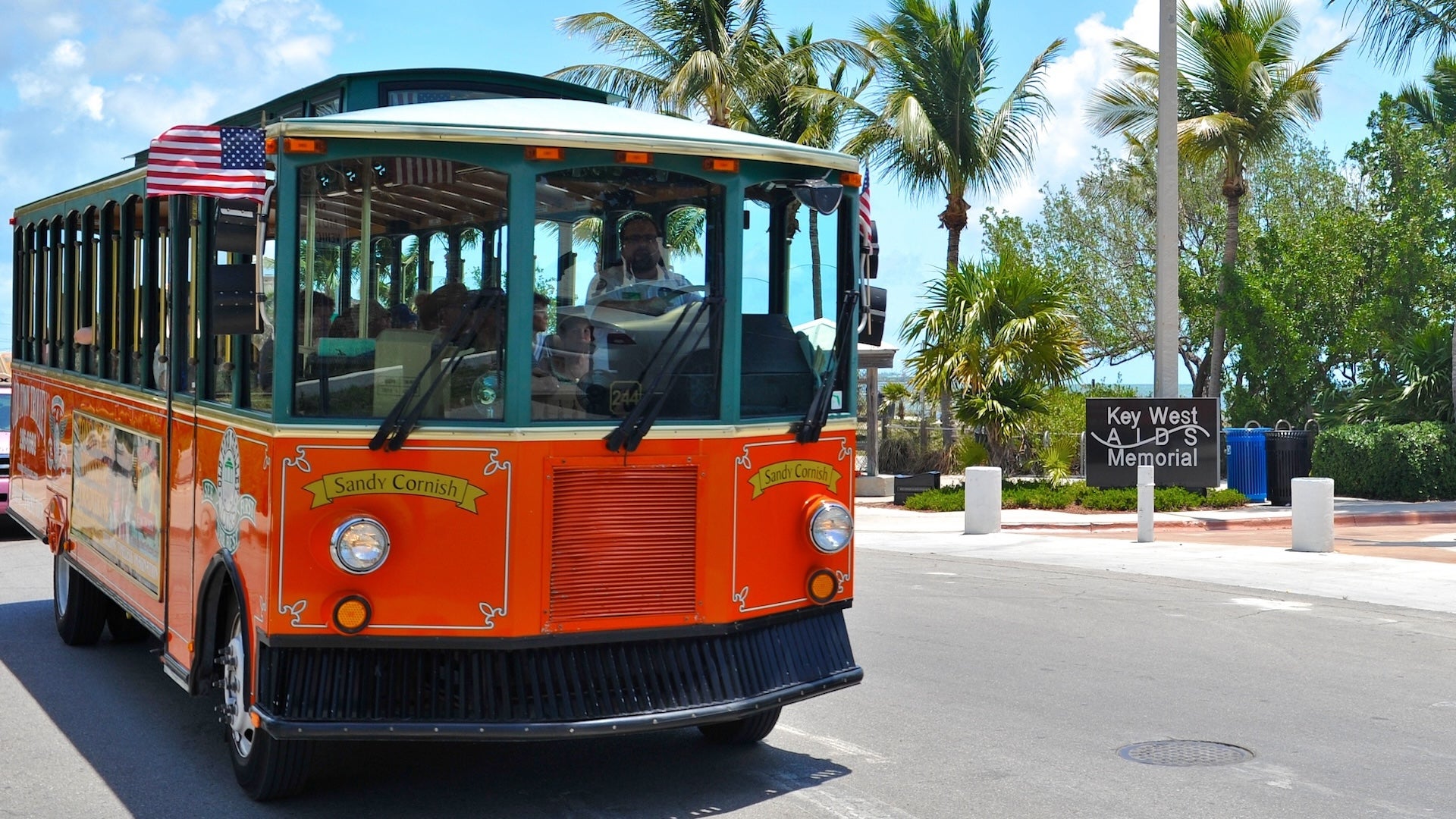 red trolley bus and its driver with the view of Key West AIDS Memorial entrance
