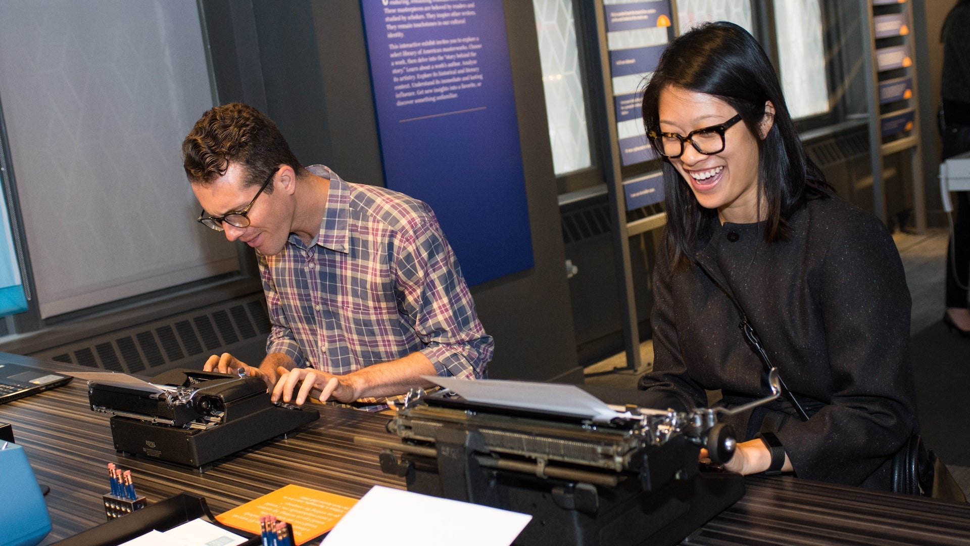 Two people using type writers at a table