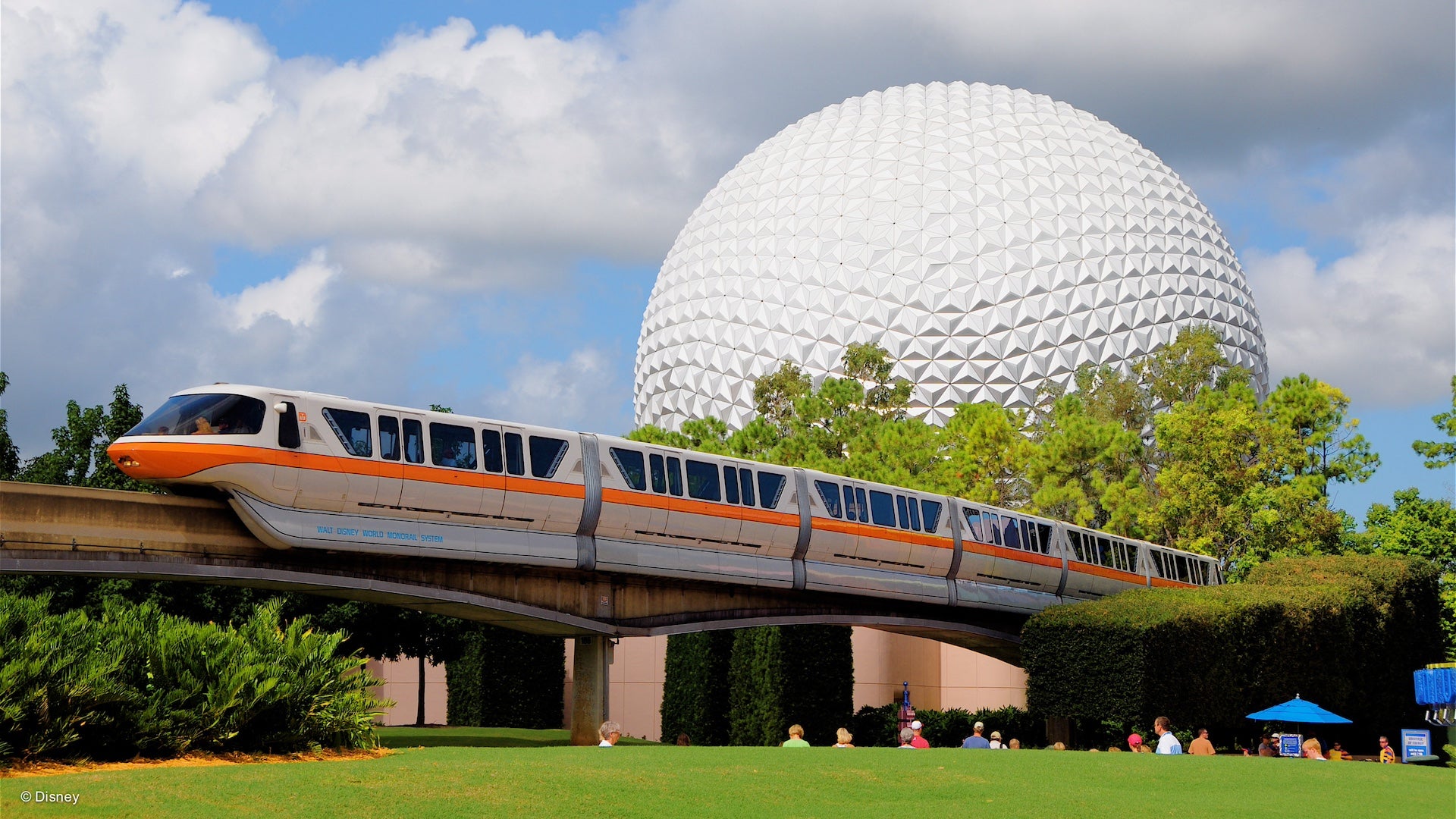 Monorail in front of Spaceship earth under a cloudy blue sky