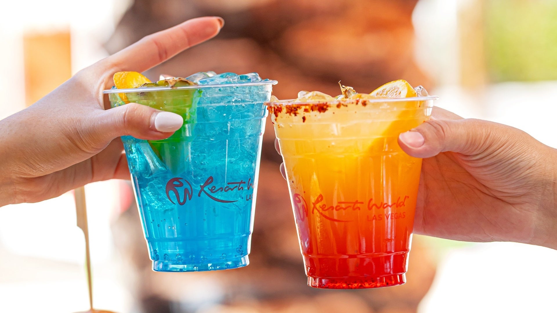 Two brightly colored cocktails with hands holding them