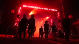 Several people walking under a neon lit sign at the entrance to Halloween Horror Nights in Orlando