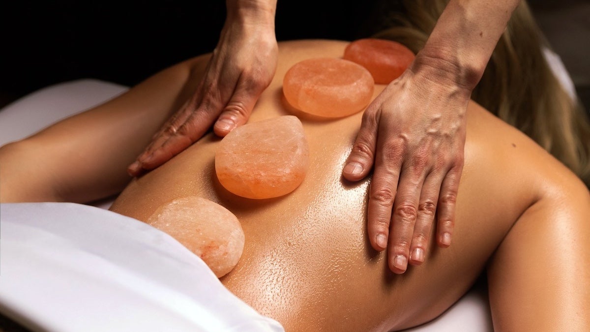 Massage therapists hands on someones back with hot stones resting on their spine as they get a massage