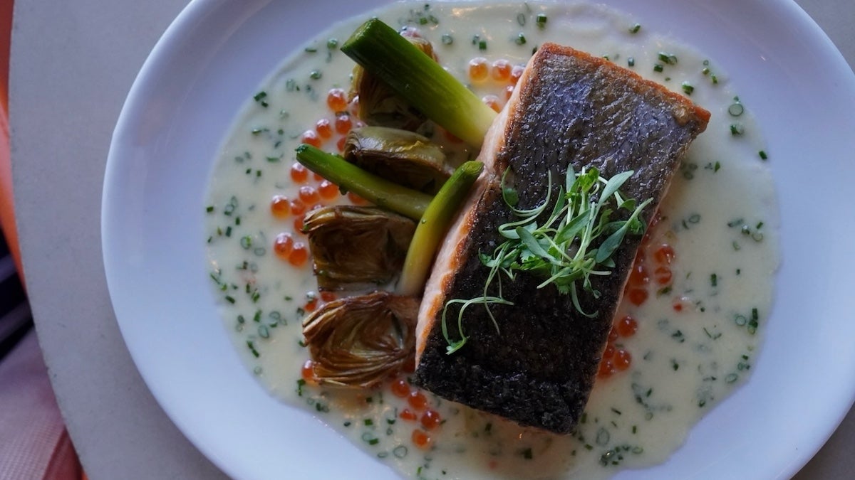 Salmon on a white plate with greens and a cream sauce