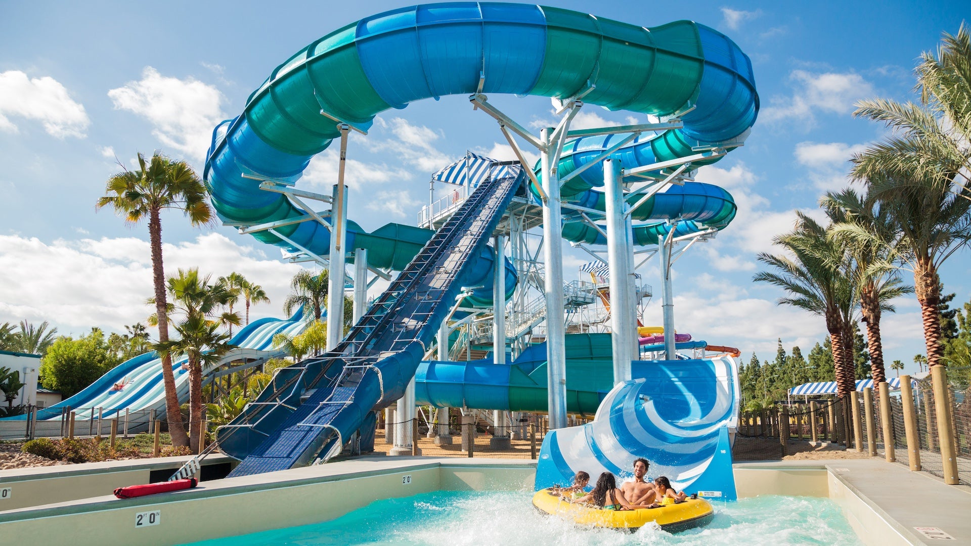 Blue and green water slide with a family in a yellow tube finishing at the bottom