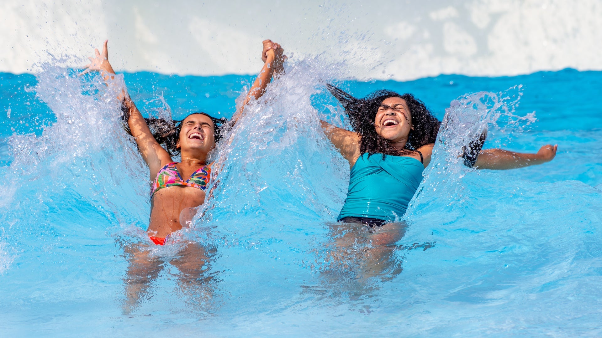 Two girls holding hands in a wave pool at Raging Waters