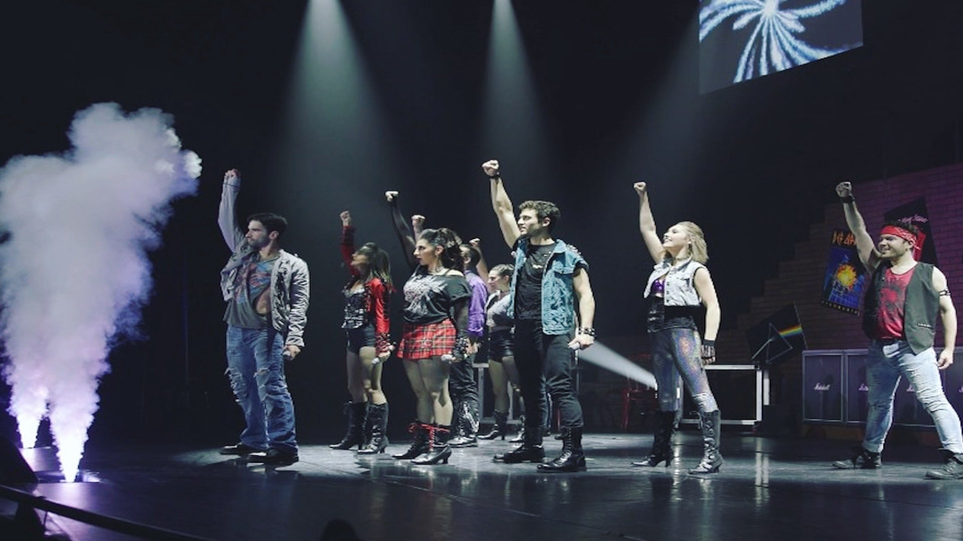 a group of performers on stage raising their right hands