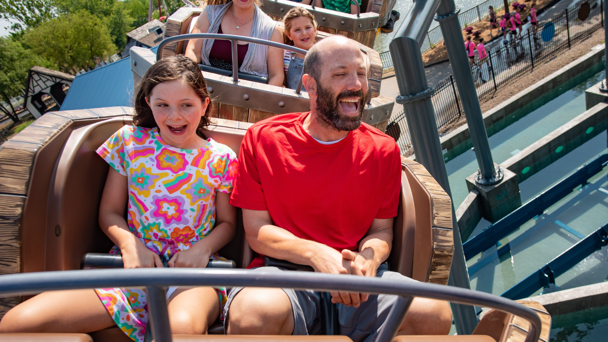 Father and daughter enjoy a thrilling ride at Adventureland, both laughing and smiling with excitement.