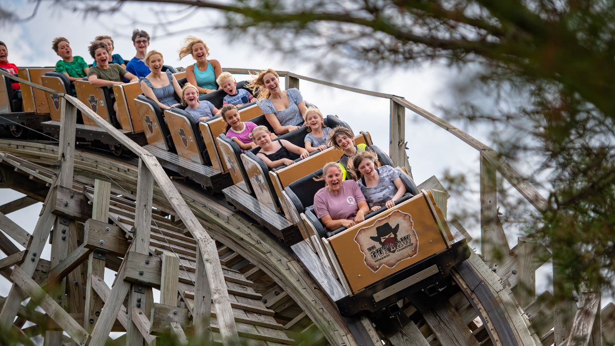 Thrill-seekers enjoy a ride on the wooden roller coaster at Adventureland, screaming and smiling with joy.