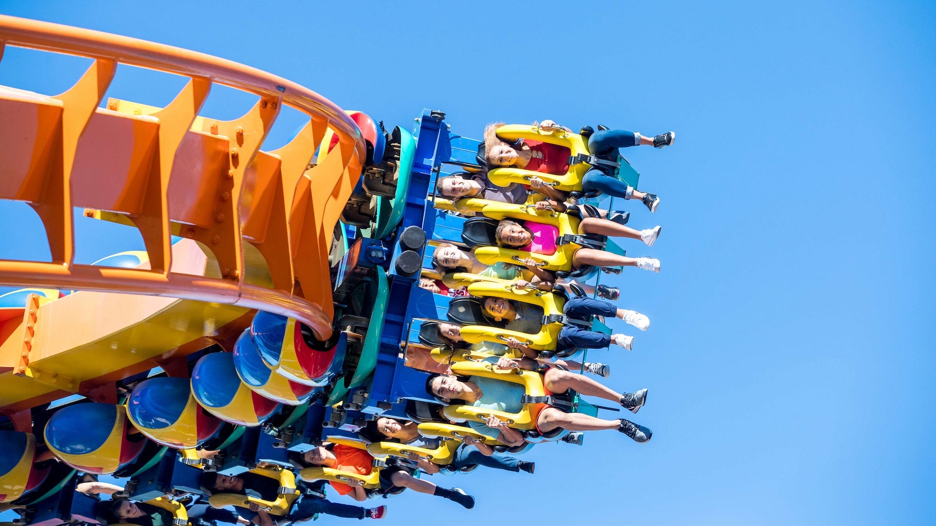 Orange roller coaster with riders strapped into a blue cart riding sideways