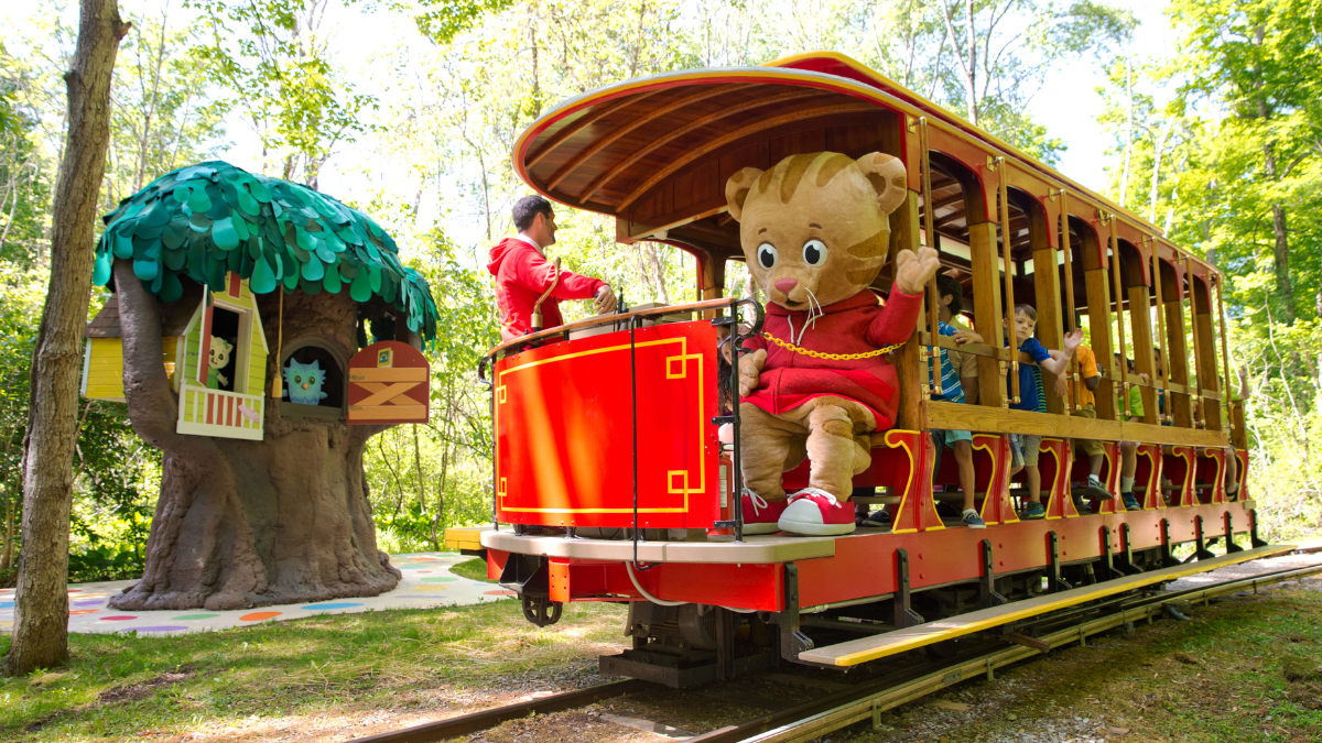 A character from Daniel Tiger’s Neighborhood waves to kids aboard the red Idlewild SoakZone train.