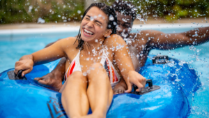 A couple laughing together as they get splashed on a blue inflatable tube.