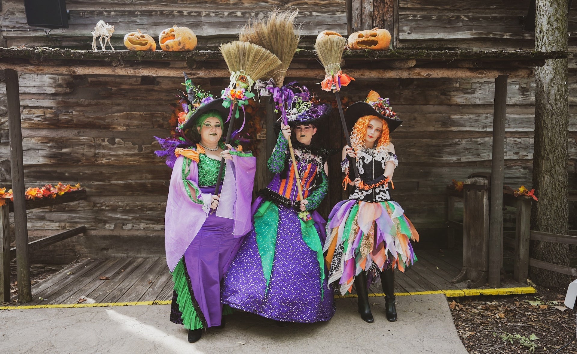 Three people dressed as witches holding broomsticks