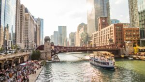 A river boat floating along a river with chicago skyscrapers along each side