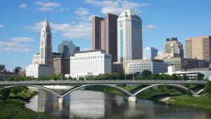 Skyline of a city under a blue sky with a bridge over a river in the foreground