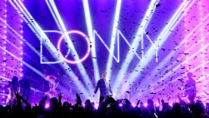 Man performing on a stage with a neon DONNY sign behind him