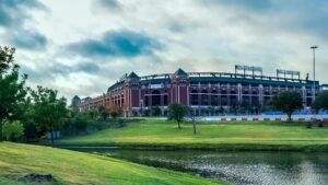 Wide shot of a ballpark in the distance with a river and grassy area in the foreground