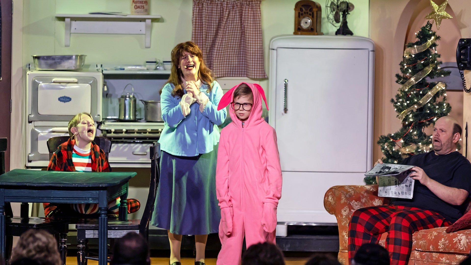 A family is in a living room set while a woman sings and a boy is in a pink bunny suit at the A Christmas Story Dinner Show