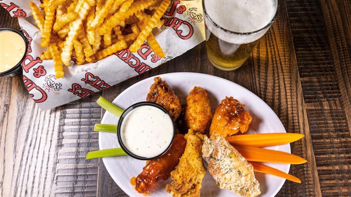 Chicken wings with celery and carrots on a plate next to a basket of fries and a glass of beer