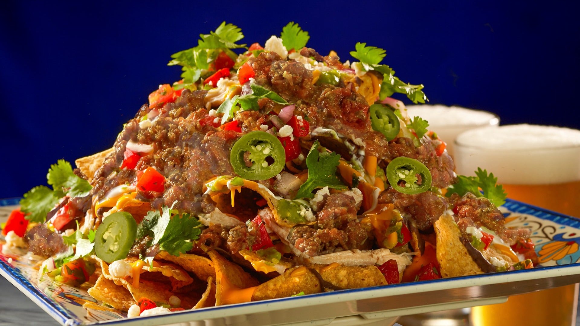 plate full of cheesy nachos with loads of toppings, beer in the back