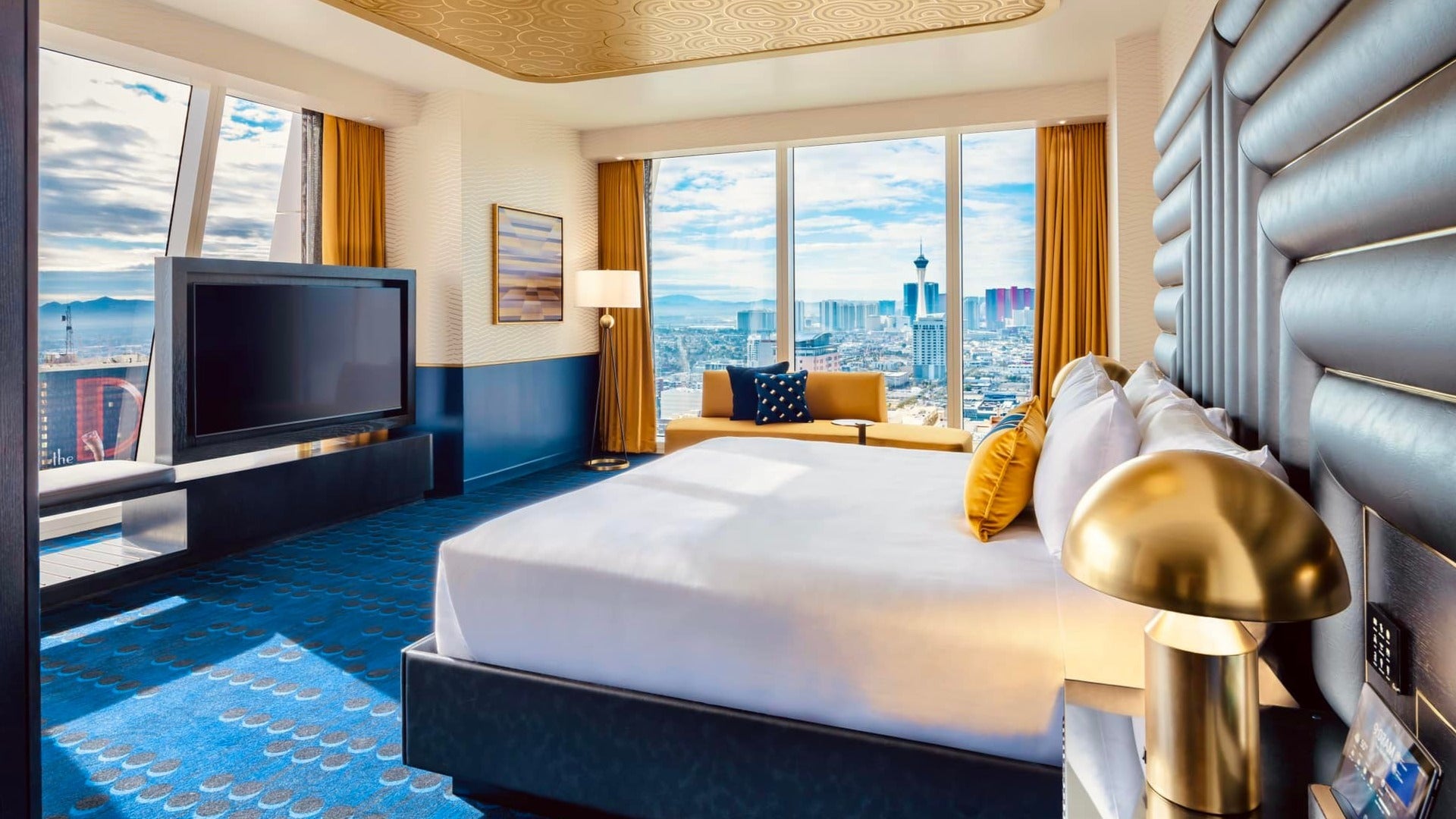 hotel room interior with bed, gold lamps, tv and view of las vegas