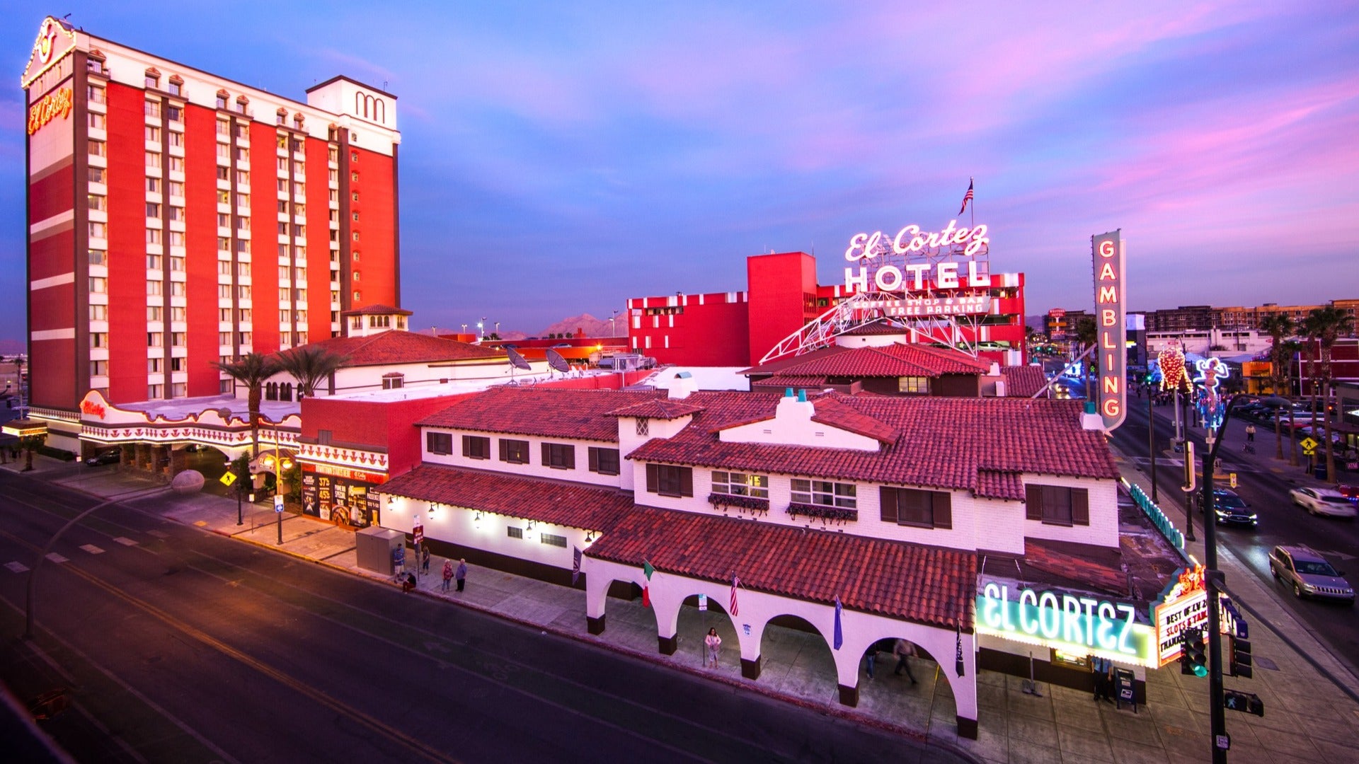 hotel exterior with people walking outside and cars driving by