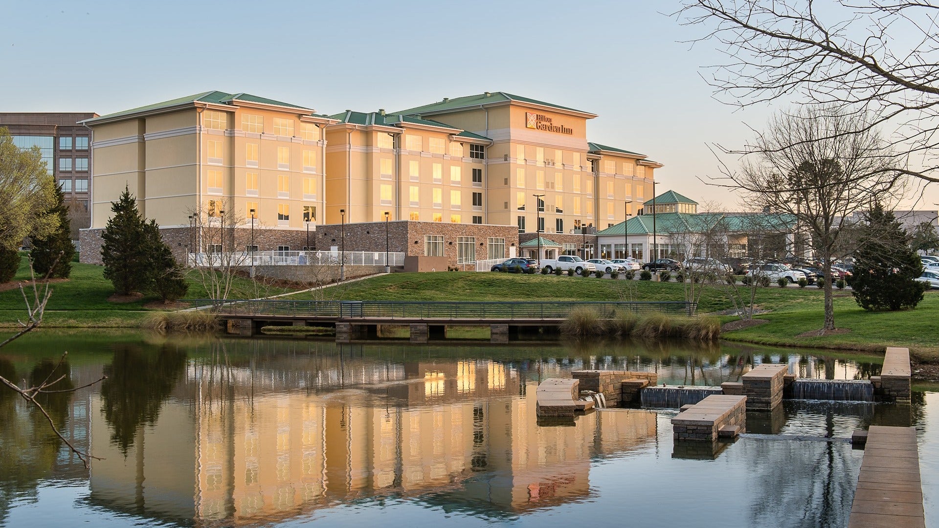 hotel exterior reflecting on a lake with cars in the parking lot