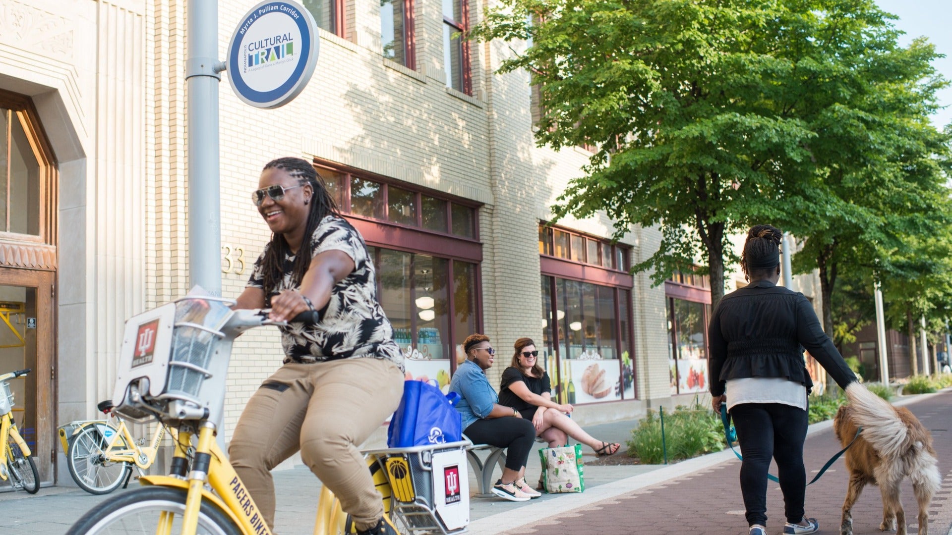 people biking, sitting and chatting, walking dog with a building at the back