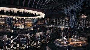 Dimly lit dining area with black walls, a dark ceiling, gold marble tables and a circle bar in the middle