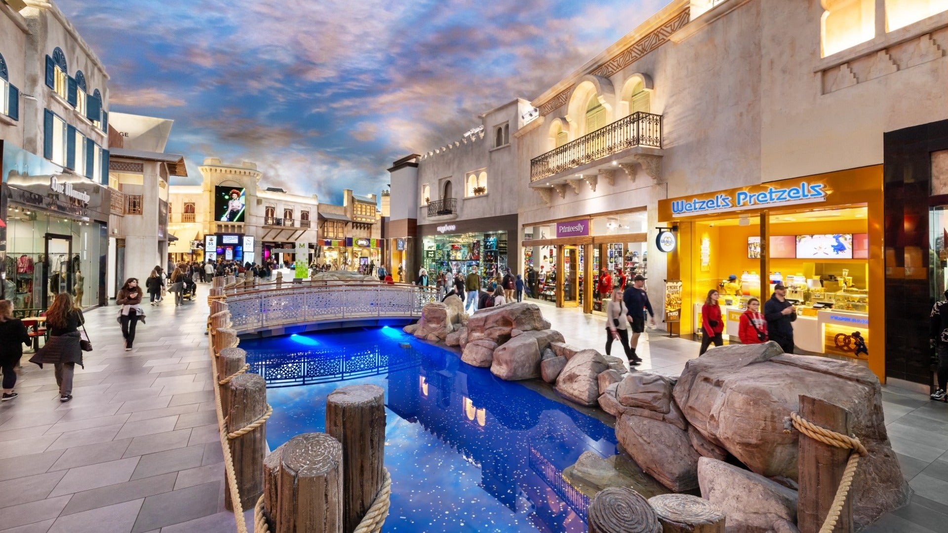 array of stores with people shopping, pond and bridge in the middle