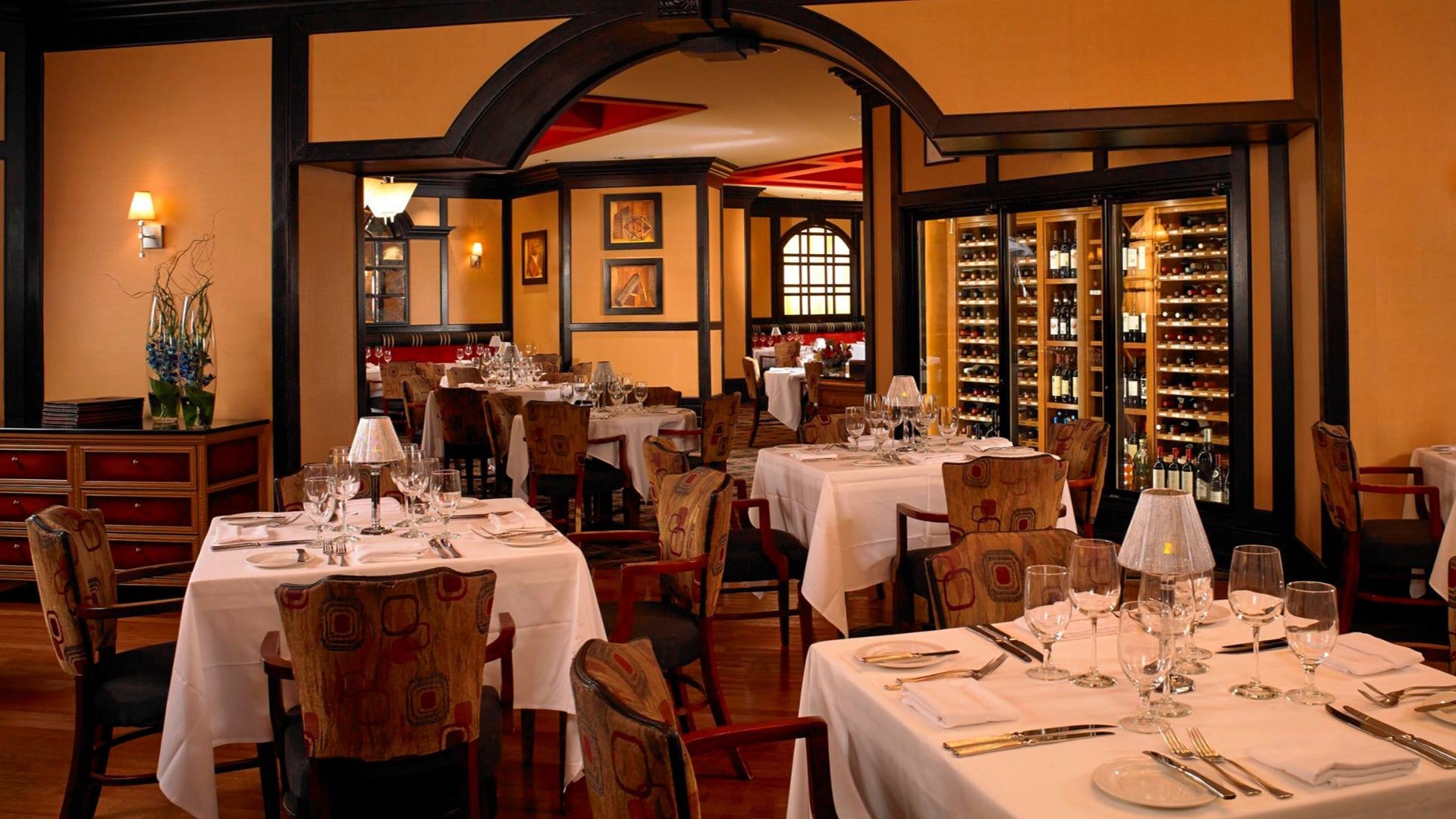 dining tables and chairs with a wine cellar at the back. wine glasses and lamps on the tables