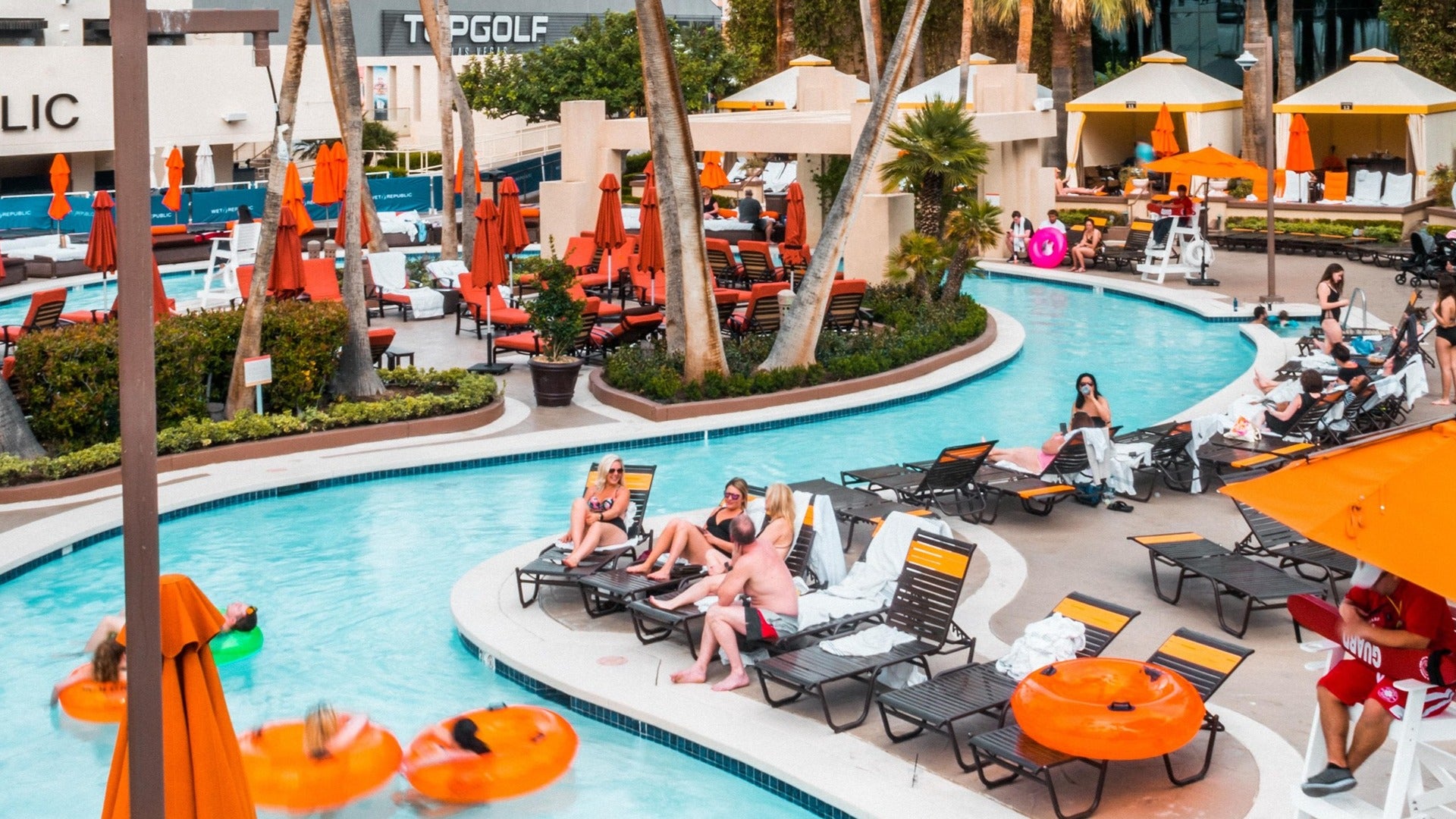 people lounging by the pool with cabanas and umbrellas