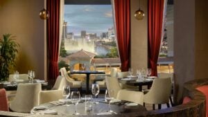 A dining area with red curtains and tables with white chairs and a window looking out over the Las Vegas strip