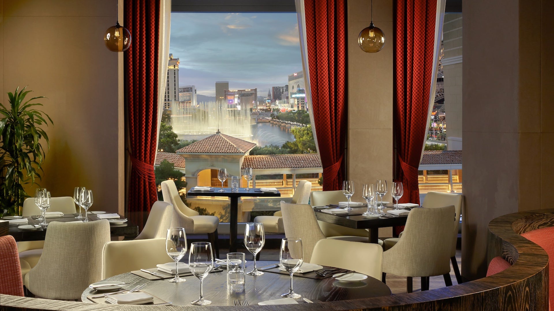 A dining area with red curtains and tables with white chairs and a window looking out over the Las Vegas strip