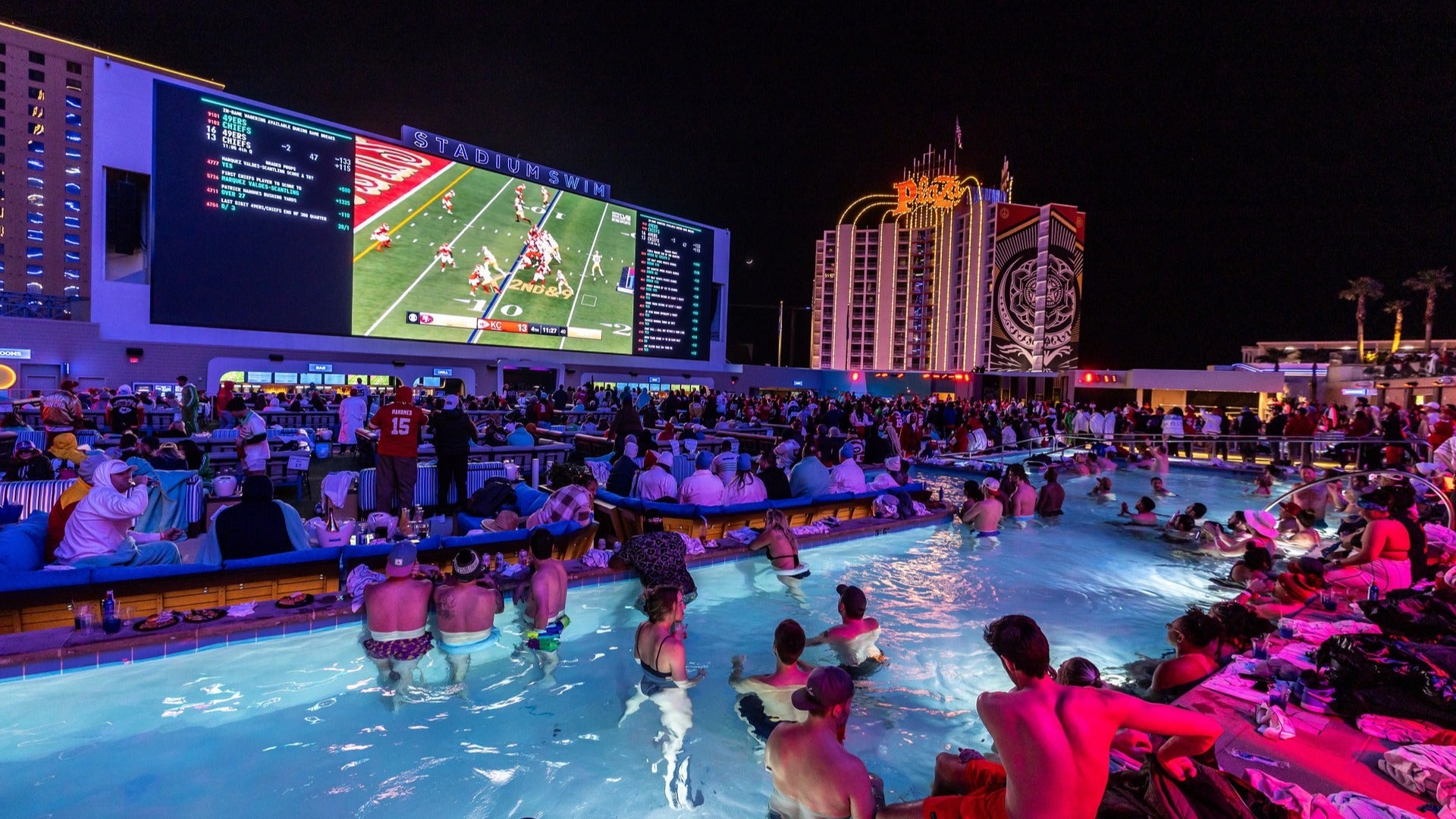 people in a pool watching a football game while partying and drinking