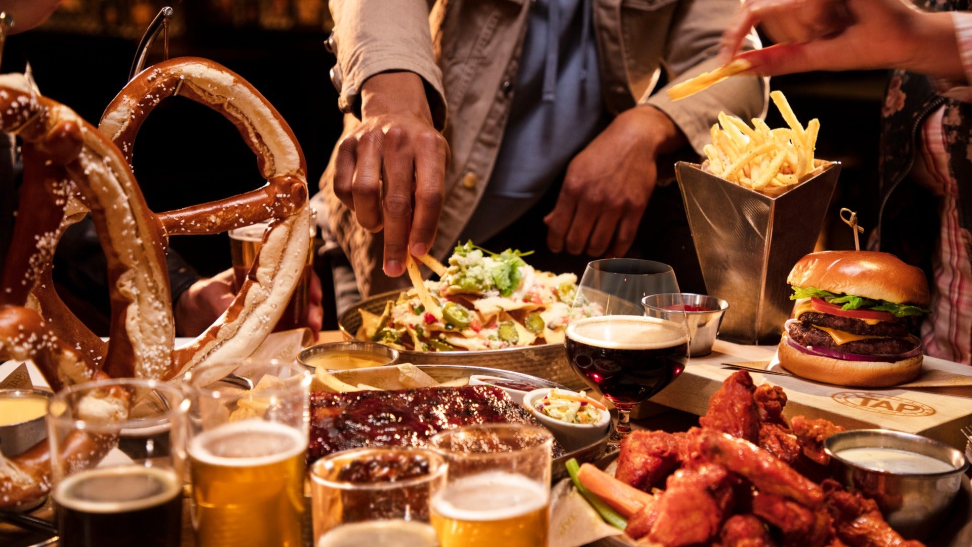 group of people enjoying food, pretzel, fries, burger, beer