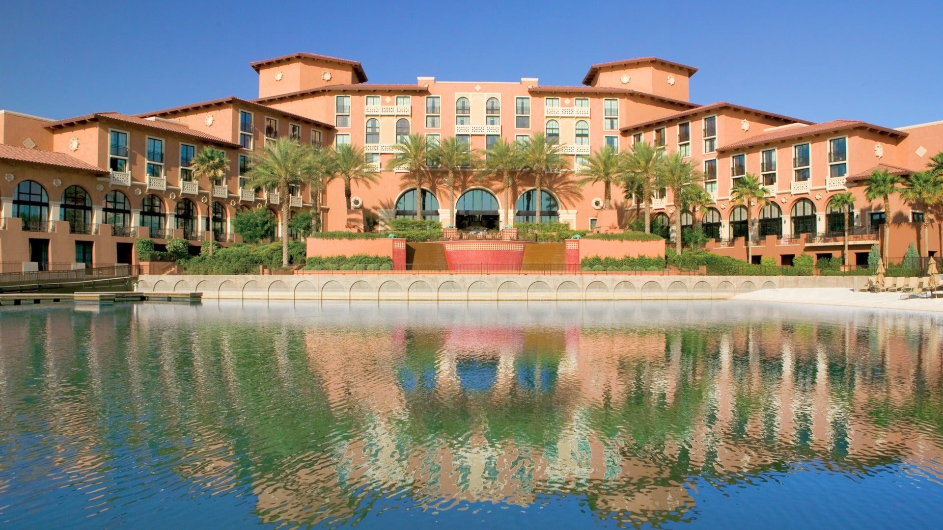 hotel exterior on a sunny day beside a lake, palm trees and tall windows