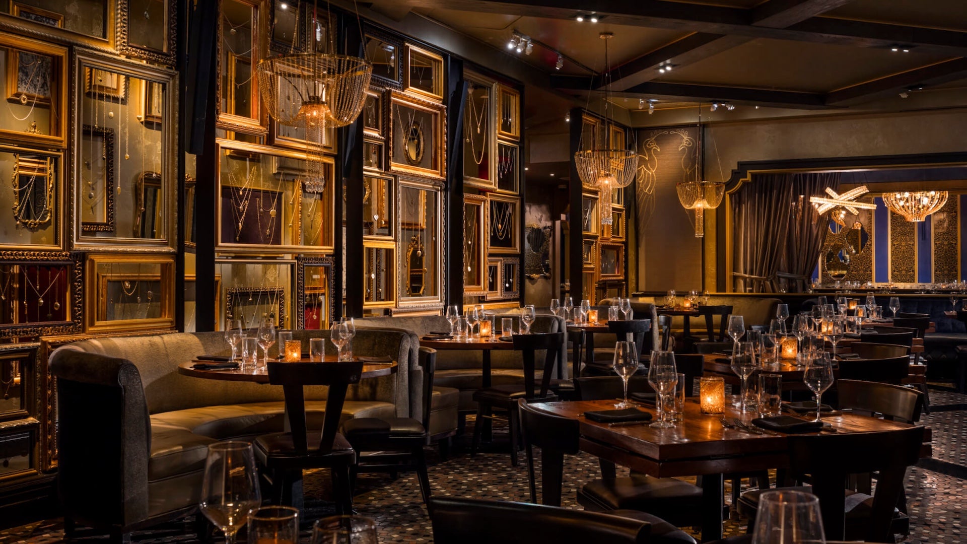 Dimly lit speakeasy style dining room with chandeliers and mirrors covering the walls