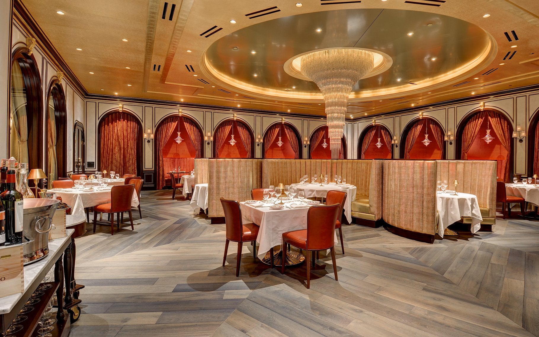 Interior shot of a dining room with a gold ceiling and dining tables with white table cloths and orange chairs