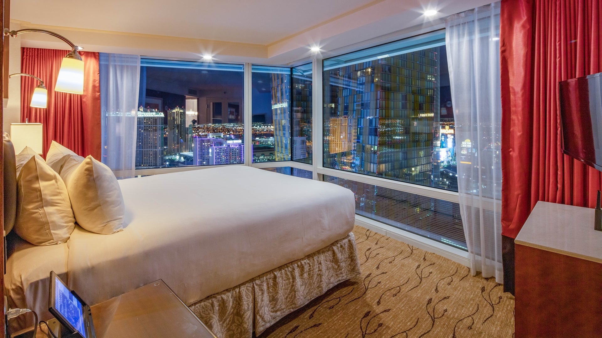 Suite in a hotel with large windows, red curtains and a bed with white and cream bedding