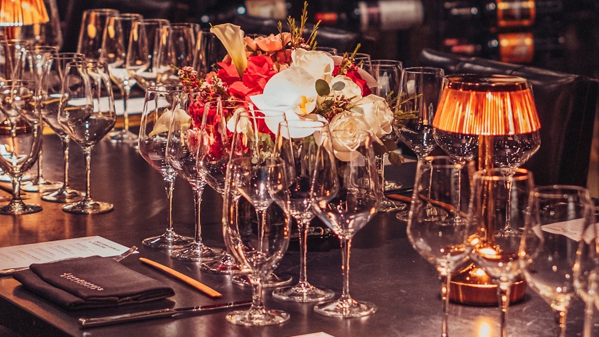 Several wine glasses on a table with a flower arrangement and dinner menu