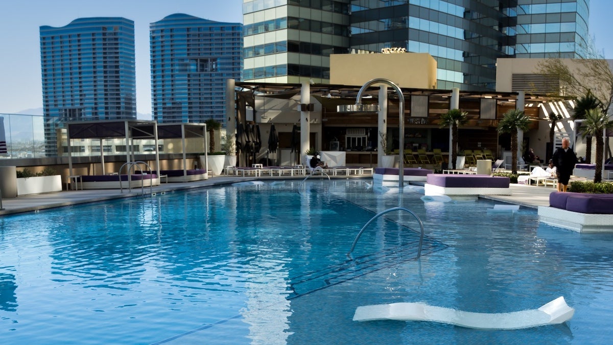 Pool with white lounge chairs and purple cushions with hotels in the background