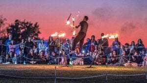 man performing stunts while juggling fire with an audience watching