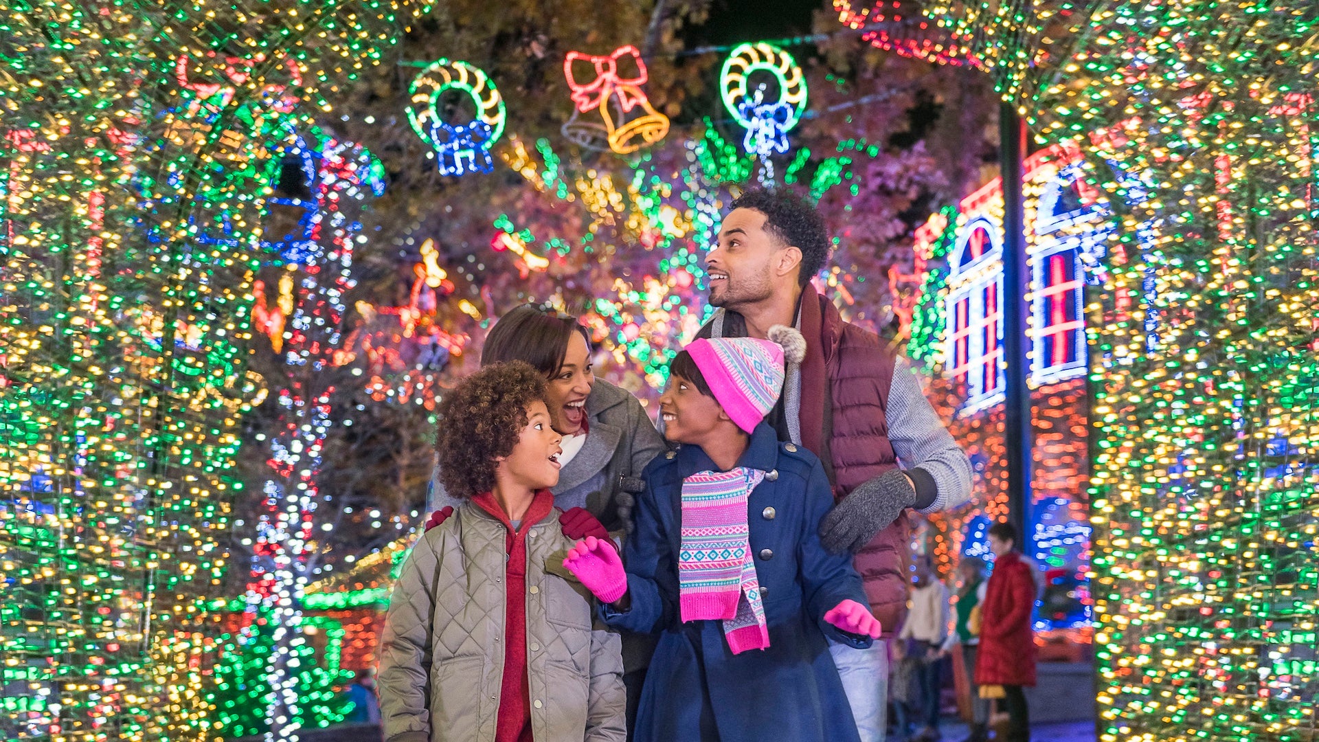 Family of four dressed in winter coats under a tunnel of christmas lights