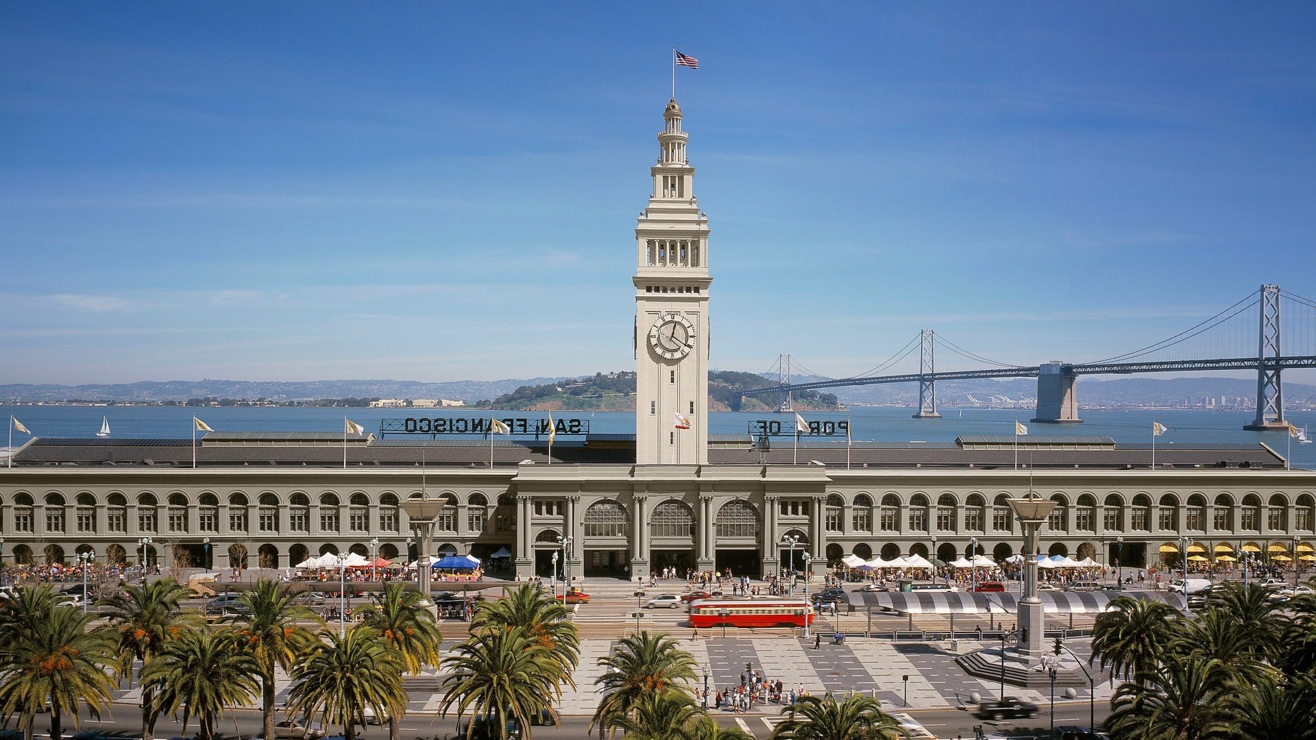 building with ocean view in the back, palm trees in front with people and cars passing by