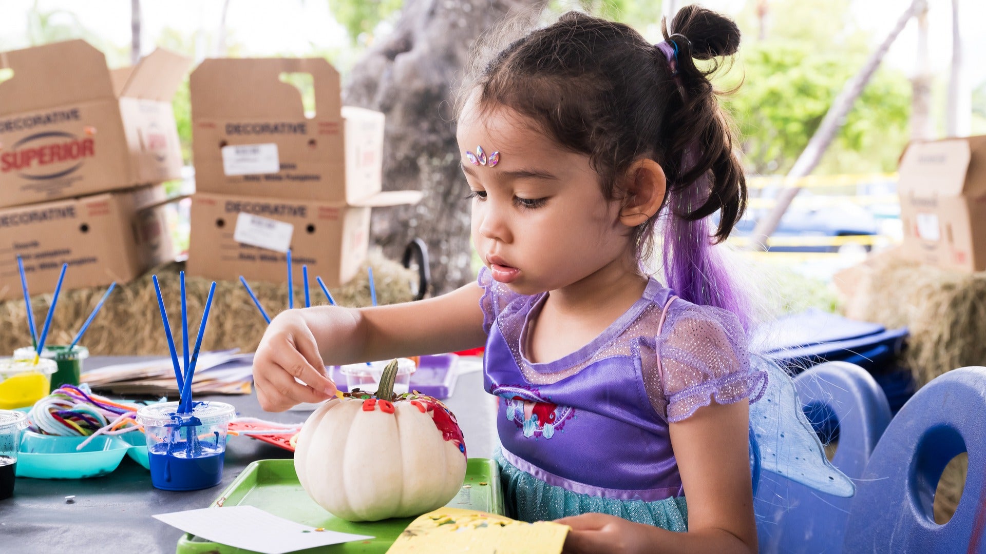 child in a costume painting a pumpkin